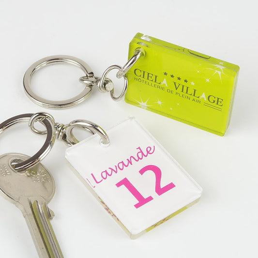 Un petit porte-clé Créoplex 40 x 30 mm posé à côté d’autres objets personnels de petite taille