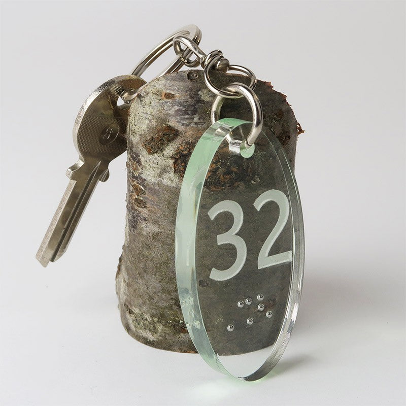 Porte-clé ovale Créolaz 6,5 cm x 3,5 cm en plexiglas transparent, avec numéro gravé en relief négatif sur la face avant, conçu pour les malvoyants.